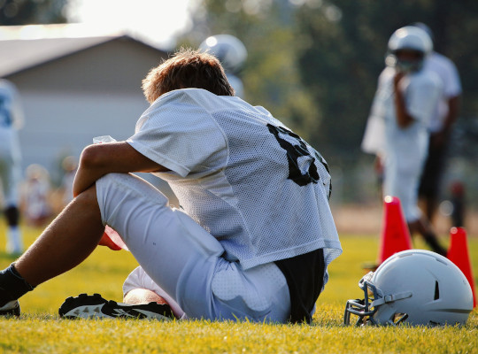 american football player sitting on ground with helmet off