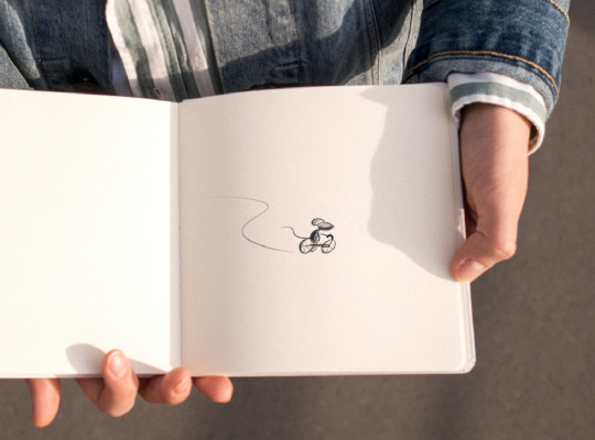 person holding sketch book with drawing of mouse on tricycle