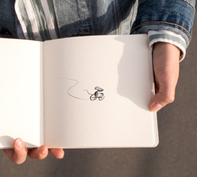 person holding sketch book with drawing of mouse on tricycle